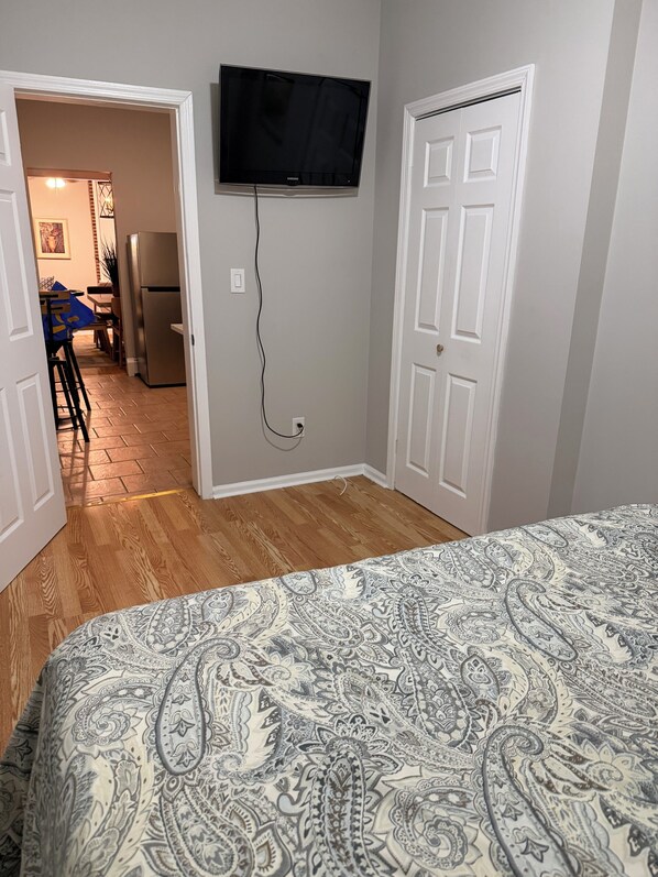 Un dormitorio con una colcha estampada, un televisor de pantalla plana montado en la pared y suelo de madera.