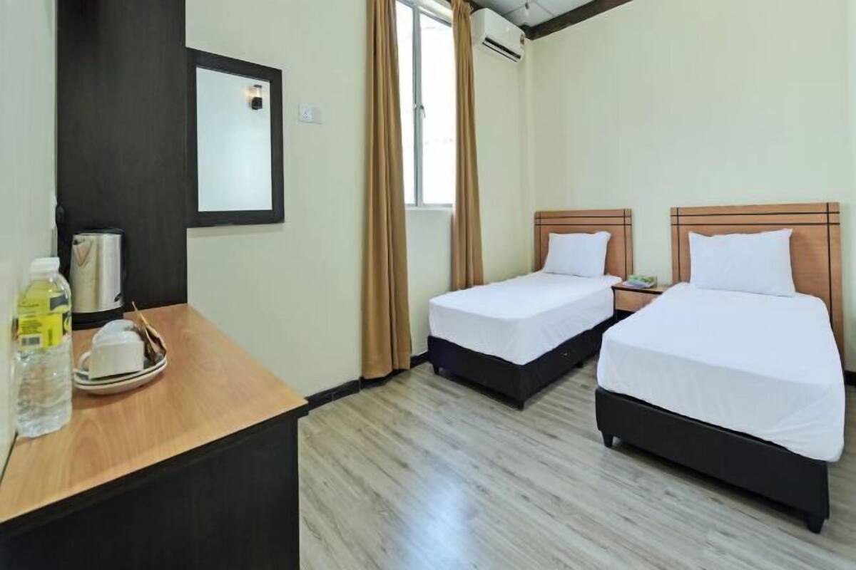 Habitación de hotel con dos camas, un escritorio de madera con una bandeja de artículos de aseo, un espejo y una ventana con cortinas.