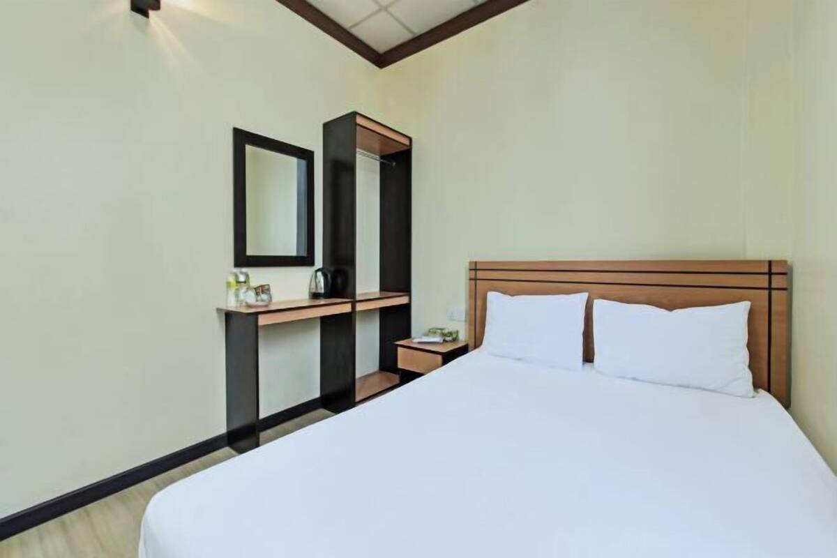 Habitación de hotel con cama, mesita de noche, espejo y armario empotrado.