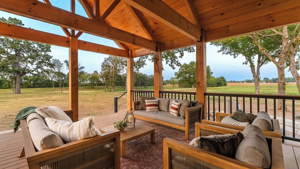 A covered outdoor seating area with wooden furniture and a view of a vineyard. - Completely renovated heritage home in the Ozarks Mountain region of SW Missouri. (Billings)