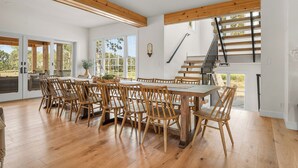 A spacious dining area with a large wooden table and chairs, a staircase with wooden railings, and large windows offering a view of the outdoors. - Completely renovated heritage home in the Ozarks Mountain region of SW Missouri. (Billings)