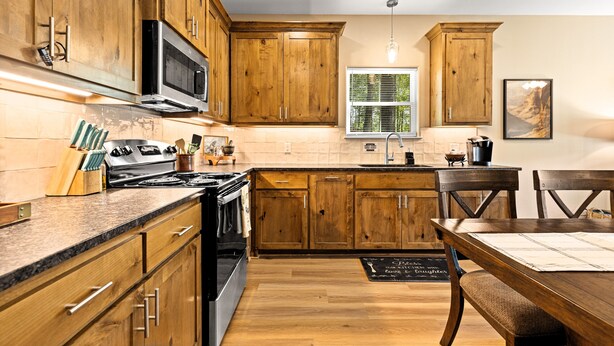 A kitchen with wooden cabinets, a stainless steel stove, and a dining area with a wooden table and chairs. - The Skelly Hideout (Kilgore)