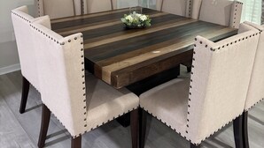 Ein Esszimmer mit einem rechteckigen Holztisch, umgeben von sechs gepolsterten Stühlen mit Knöpfen. Auf dem Tisch steht eine Vase mit getrockneten Pflanzen, und an der Wand hängt ein Spiegel.