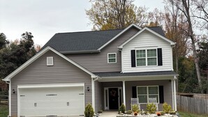 Ein zweistöckiges Haus mit Garage, einer Veranda und einem gepflegten Rasen.