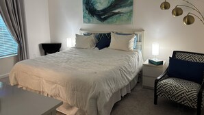 A neatly arranged bedroom with a large bed, a bedside table with a lamp, a chair, and a painting on the wall. - 3/2 Villa in most desired Richmond neighborhood in the Villages. Jan-Apr rental (The Villages)