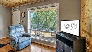 Une pièce avec une grande fenêtre, un canapé bleu, une télévision et une pancarte sur laquelle on peut lire : « LEVEL UP STAYS ».