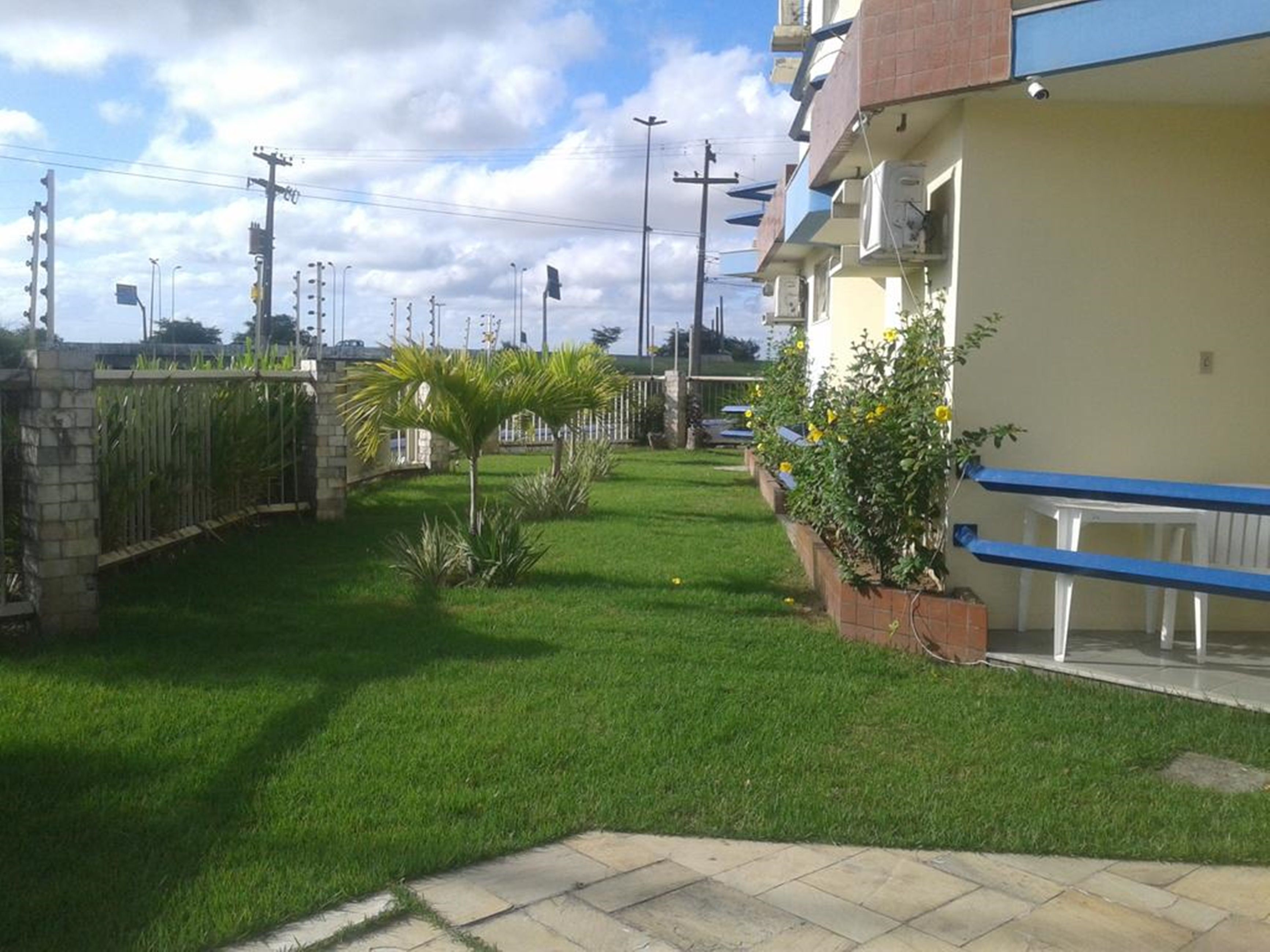 Zona residencial con césped cuidado, una palmera y un edificio con barandilla azul.