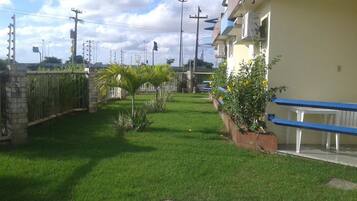 Zona residencial con césped cuidado, una palmera y un edificio con barandilla azul.
