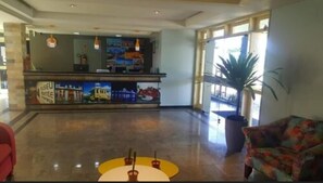 A hotel lobby with a reception desk, a large potted plant, and a colorful armchair. - Rede Andrade Aracaju (Aracaju)