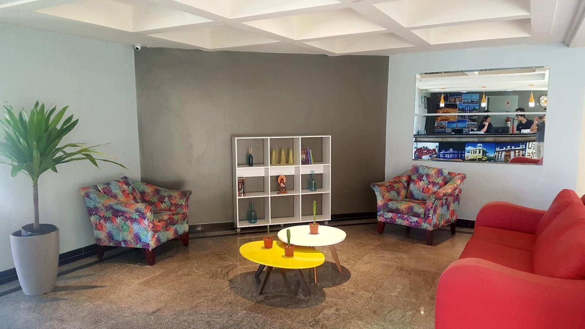Um hall moderno com dois poltronas estampadas, um sofá vermelho, uma pequena mesa amarela e um aparador branco com objetos decorativos.