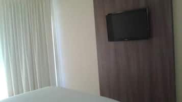 Una habitación de hotel con una cama, un televisor montado en un panel de madera y una ventana con cortinas.