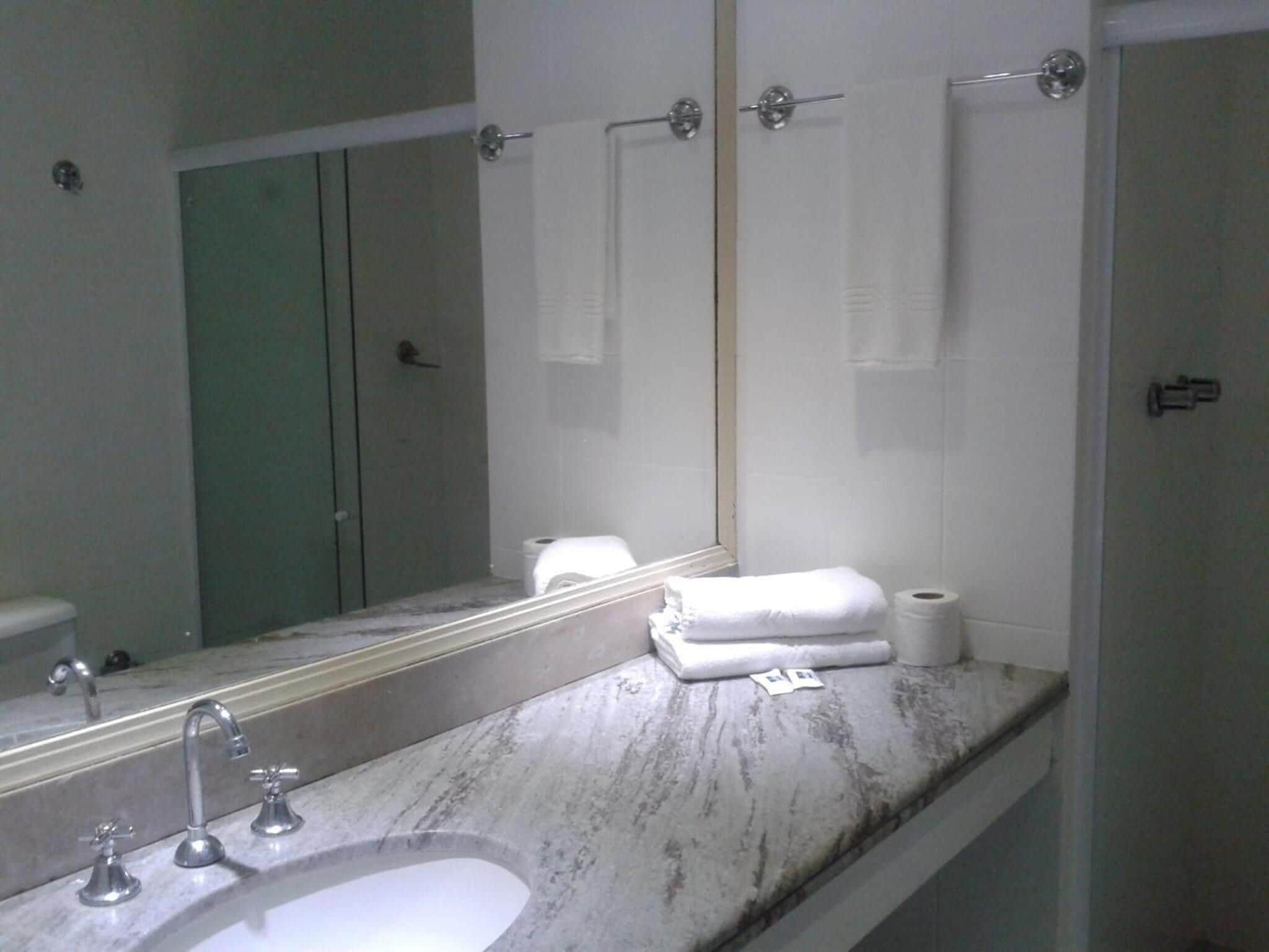 A bathroom with a marble sink, two faucets, a mirror, and a towel rack with towels.
