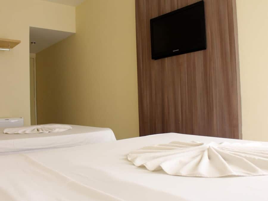 Habitación de hotel con dos camas, un televisor de pantalla plana montado en la pared y detalles de paneles de madera.