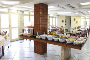 A buffet setup with various food items, a brick pillar, and a tiled floor.