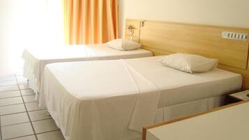 A hotel room with two single beds, a wooden headboard, a small bedside table, and a window with curtains.