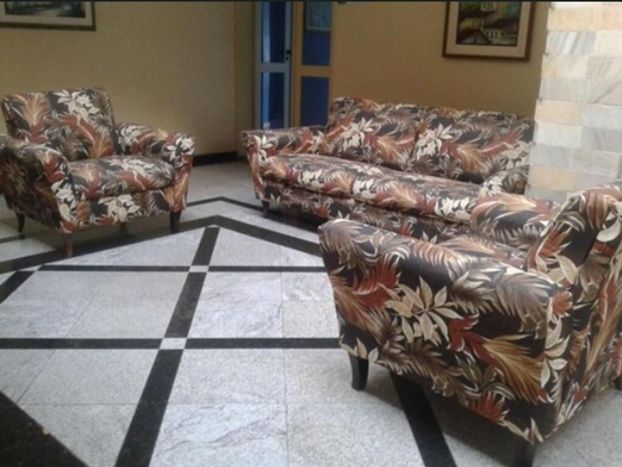 A lobby with a checkered floor, floral-patterned sofas, and a door in the background.