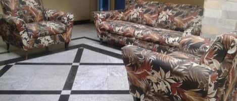 Un vestíbulo con suelo a cuadros, sofás estampados con motivos florales y una puerta al fondo.