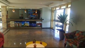 A hotel lobby with a reception desk, a large potted plant, and a colorful armchair. - Rede Andrade Aracaju (Aracaju)