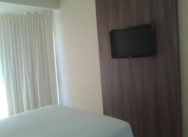 A hotel room with a bed, a TV mounted on a wooden panel, and a window with curtains. - Rede Andrade Aracaju (Aracaju)