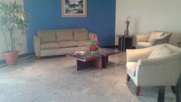A living room with a beige sofa, a white armchair, a coffee table with a vase of flowers, and a potted plant.