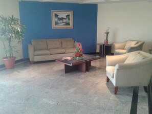 Ein Wohnzimmer mit einem beigen Sofa, einem weißen Sessel, einem Couchtisch mit Blumen und einer Zimmerpflanze.