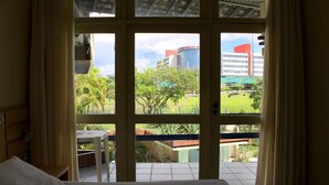 Habitació d'hotel amb llit, taula petita i vista a un edifici i vegetació a l'exterior.