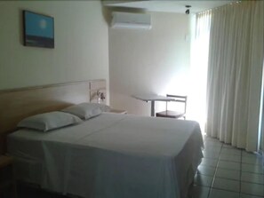 Una habitación de hotel con una cama, una mesita y un ventanal con cortinas.