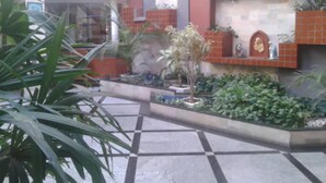 A courtyard with a tiled floor, potted plants, and a stone wall with decorative elements. - Rede Andrade Aracaju (Aracaju)