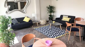 A modern living room with a black sofa, a round coffee table, and a dining table with chairs. There is a large mirror on the wall, a potted plant, and a patterned rug. - Hotel Cullera Coast by Mij (Cullera)