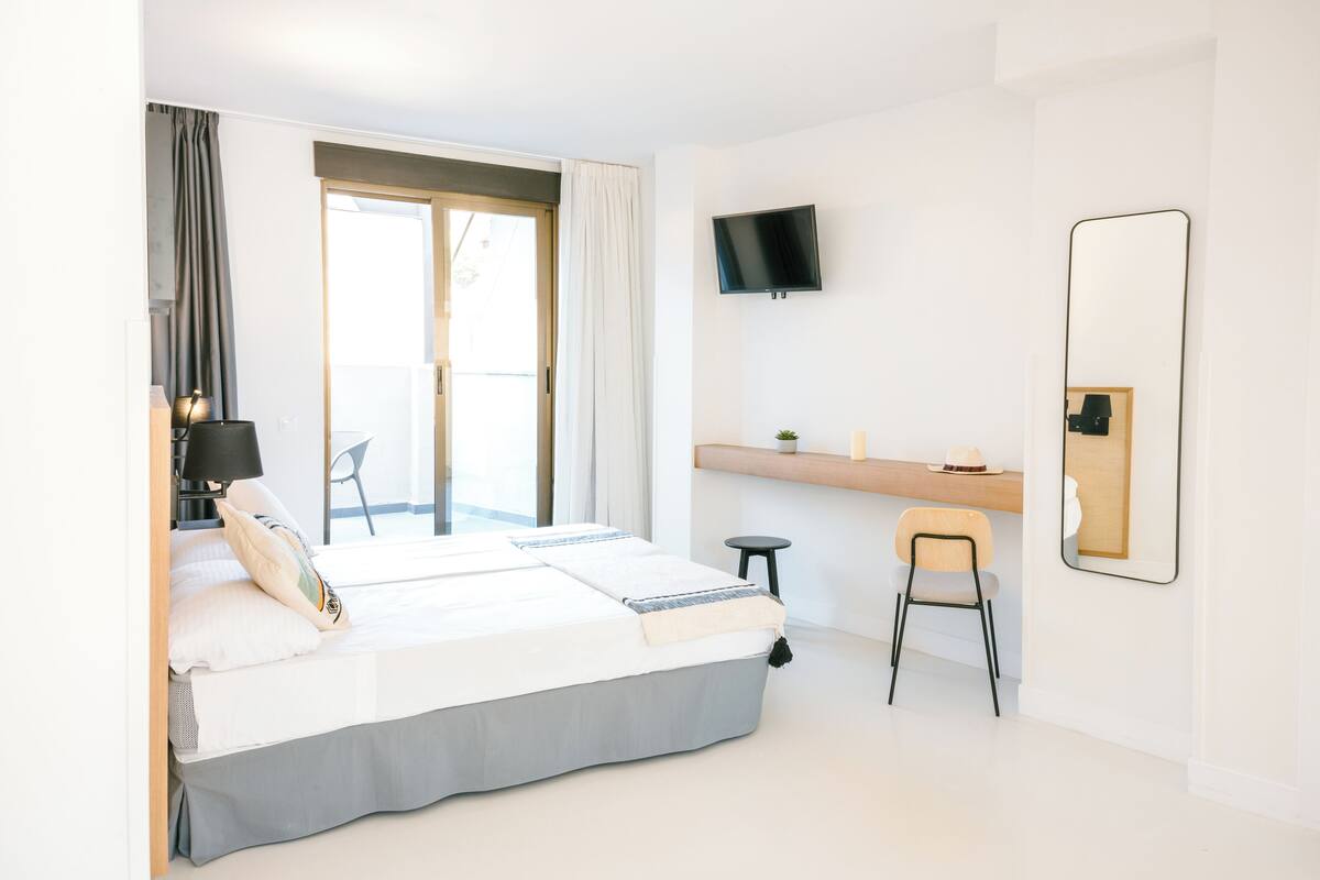 A modern hotel room with a large bed, a desk, a chair, a TV, and a large mirror.