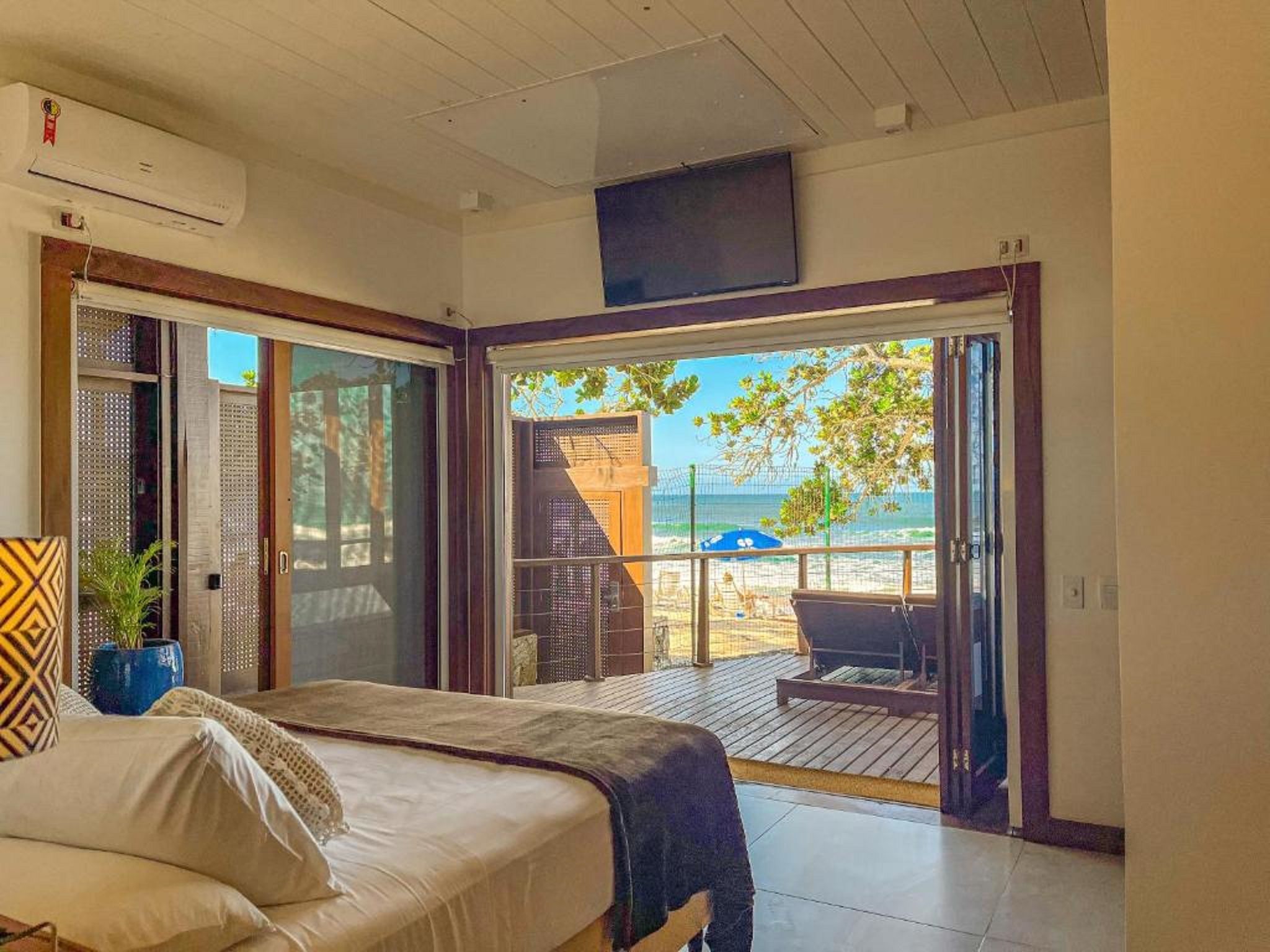 Un dormitorio con cama, televisor y vista a la playa a través de un ventanal corredera.