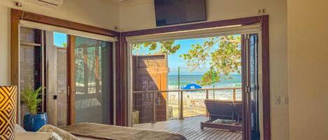 Un dormitorio con cama, televisor y vista a la playa a través de un ventanal corredera.