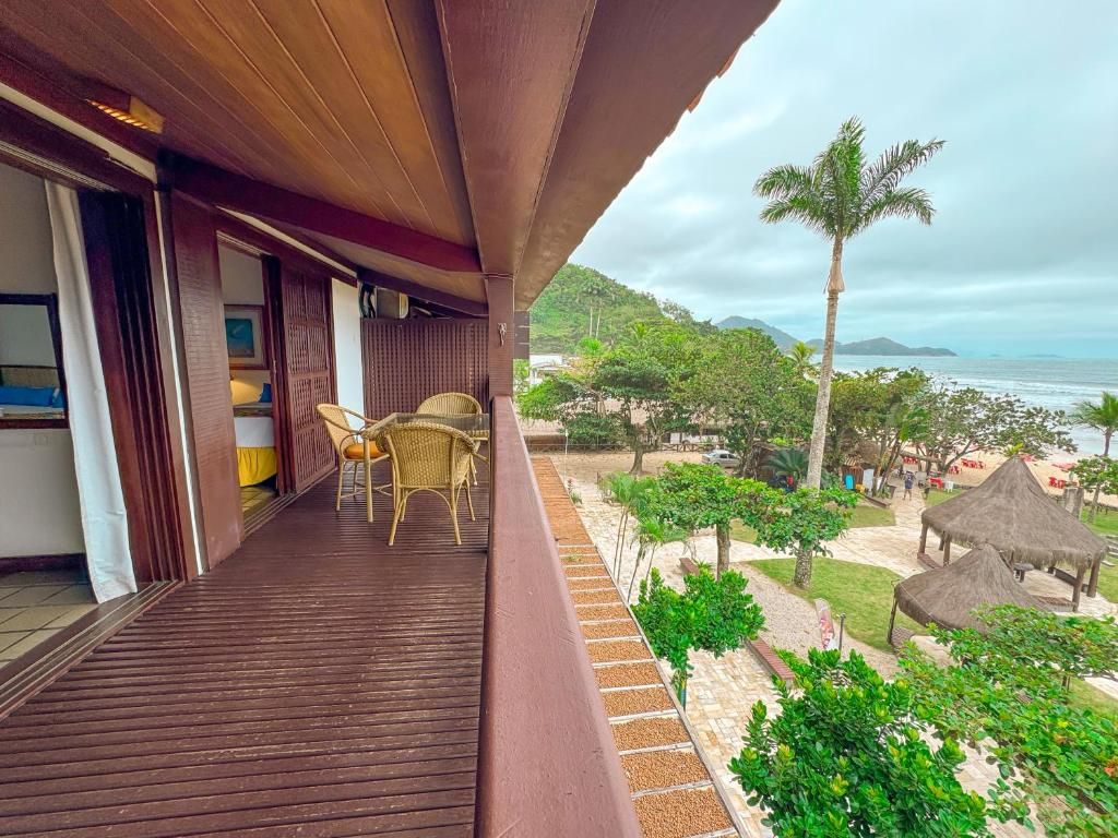 A balcony with a wooden floor, wicker chairs, and a view of the beach and palm trees.