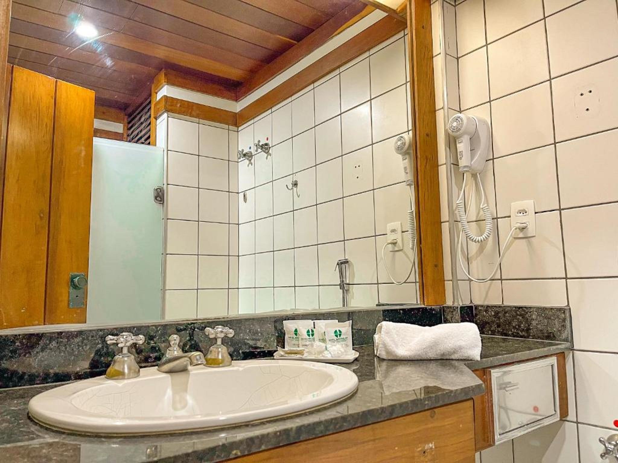 Een badkamer met een wit wastafelmeubel, een spiegel, een douche en een aan de muur bevestigde haardroger.