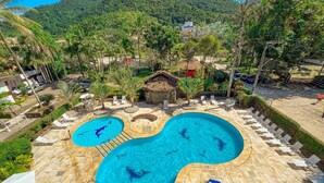 A pool area with two separate pools, lounge chairs, and a thatched-roof hut.