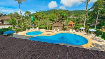Um resort com uma piscina grande, espreguiçadeiras e um bangalô com telhado de palha.
