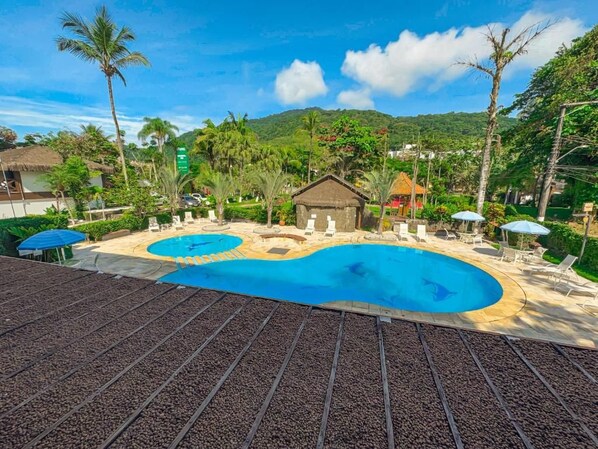 Un resort con una amplia piscina, sillas de descanso y una cabaña con techo de paja.