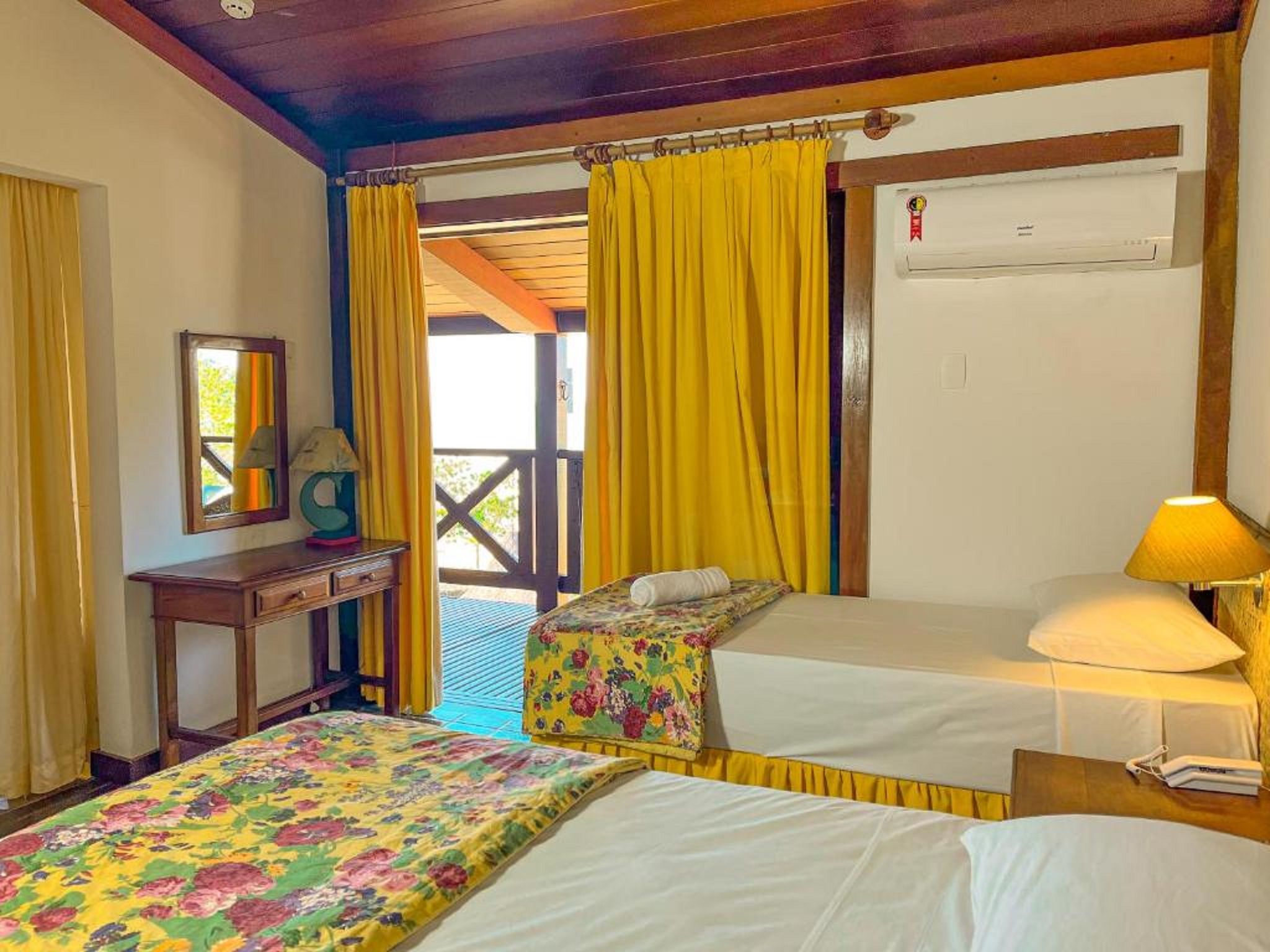 A hotel room with two beds, a desk, and a window with yellow curtains.