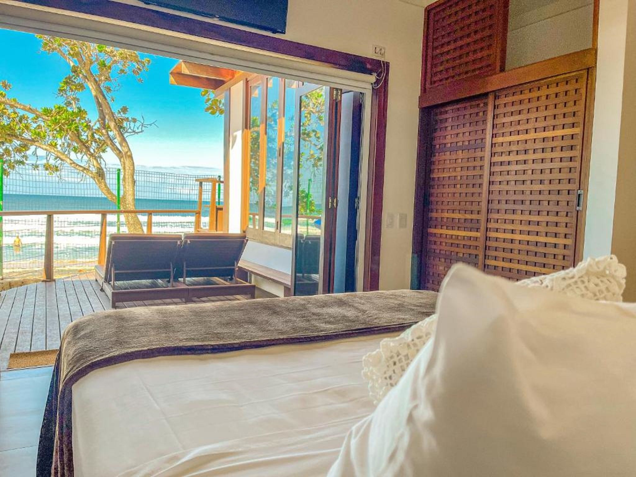 Quarto com cama, vista para a praia e varanda com mesa e cadeiras.