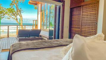 Een slaapkamer met een bed, uitzicht op zee en een balkon met een tafel en stoelen.