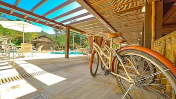 Uma área externa coberta com piscina, espreguiçadeiras e bicicletas.