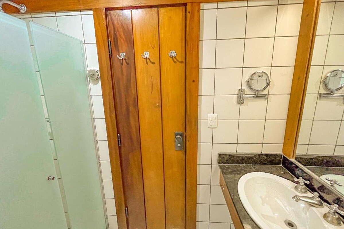 Un baño con puerta de madera, lavamanos blanco y espejo.