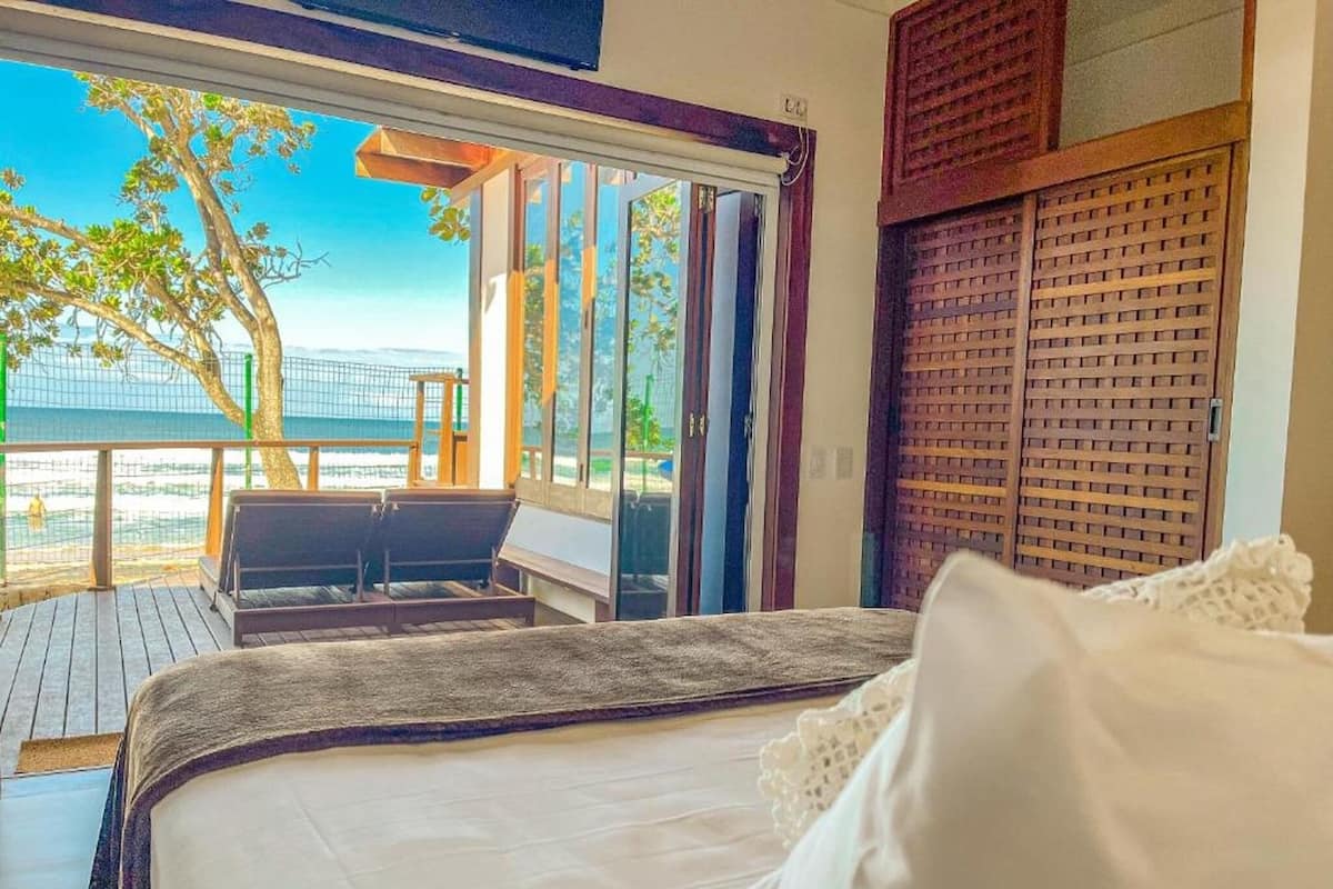 Une chambre avec un lit, une vue sur la plage et un balcon équipé d’une table et de chaises.