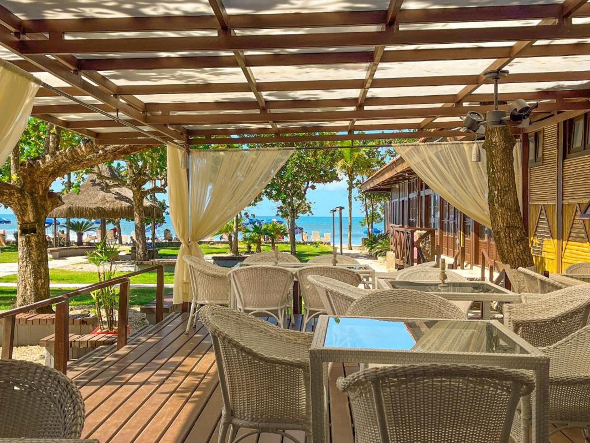 Een overdekt terras met rieten meubels, een glazen tafel en uitzicht op de oceaan.