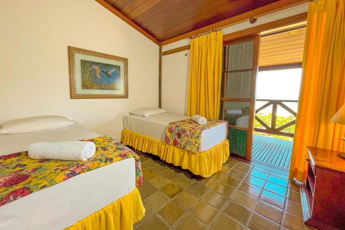 Habitación de hotel con dos camas, un cuadro en la pared y un balcón con cortinas amarillas.