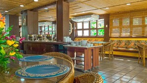 A restaurant with a tropical theme, featuring a bar area, seating with woven chairs, and a decorative ceiling.