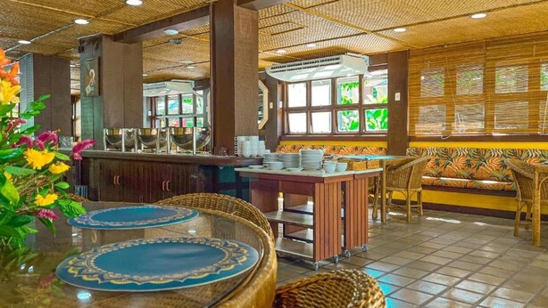 Un restaurante de temática tropical, con barra, asientos de sillas tejidas y techo decorativo.