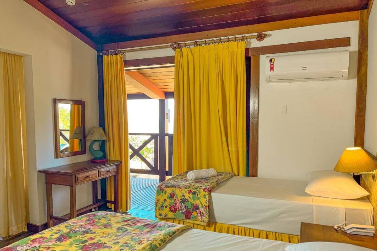 Une chambre d’hôtel avec deux lits, un bureau et une fenêtre avec des rideaux jaunes.