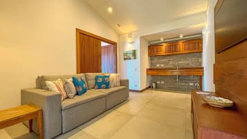 Una sala de estar moderna con un sofá gris, un banco de madera y una cocina con armarios de madera y un salpicadero de piedra.