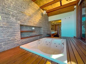 A spa area with a wooden deck, a stone wall, and a large hot tub. - Hotel Nacional Inn Ubatuba Praia Das Toninhas (Ubatuba)
